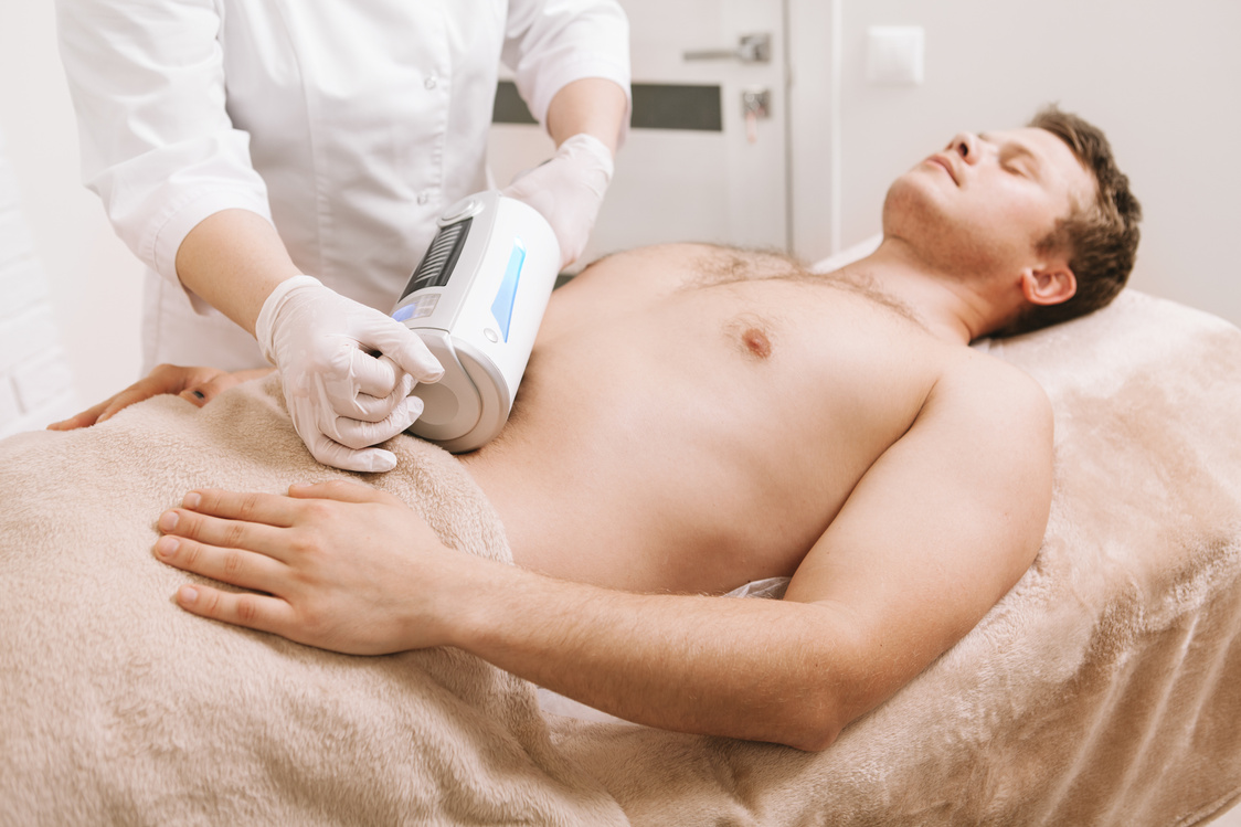 Male client relaxing while professional therapist using endospheres massaging device on his stomach